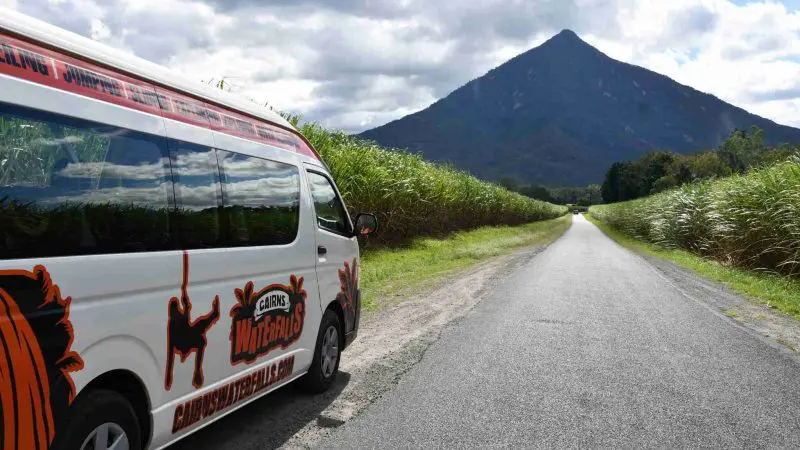 Explorer Tour van parked on a scenic rural road, surrounded by lush grassy fields and a majestic mountain in the background.