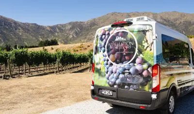 Appellation Wine Tours van parked next to lush vineyard with scenic mountains, highlighting boutique wine experiences in the region.
