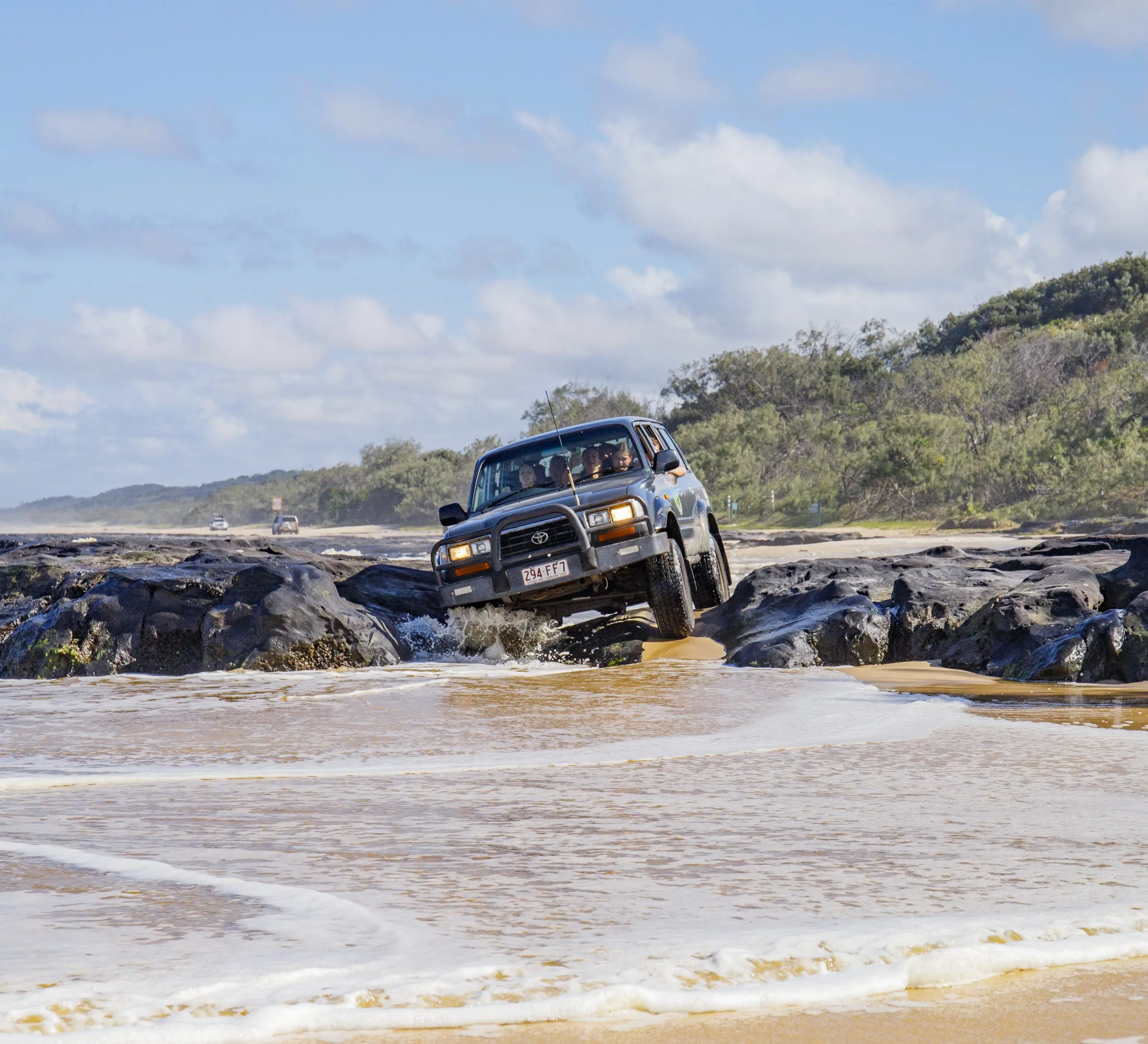 Black 4WD navigating rugged coastal rocks on a 3-Day K’gari adventure tour with dormitory accommodation, Rainbow Beach, Australia.