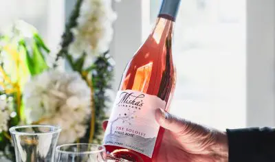 Hand displaying Misha’s Vineyard rosé wine next to elegant flowers and a decanter—ideal for luxury wine tours and tasting events.