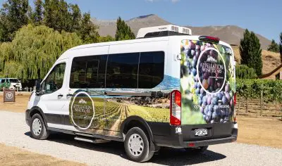 A branded white van featuring vineyard graphics on a gravel track, promoting Appellation Wine Tours’ renowned Classic Wine Tour experience.
