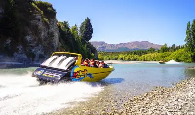 Experience the thrill of a yellow jet boat racing on a crystal-clear river, framed by scenic mountains and lush trees—ideal for an unforgettable jet boat and boutique winery tour adventure.