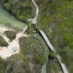 Stunning aerial shot of winding wooden boardwalk on Kgari 2 Day Tour, Rainbow Beach; swimmers relax in creek surrounded by lush trees.