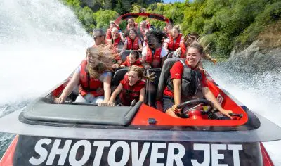 Tourists on the Shotover Jet in Queenstown experience an exhilarating jet boat ride, splashing through water in safety life jackets.