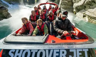 Adventurers on a Shotover Jet speed through Queenstown’s scenic canyon, water spraying as they experience New Zealand’s top thrill ride.
