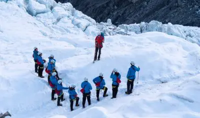 Climbers in blue jackets explore the stunning snowy terrain of Franz Josef Glacier on a guided glacier tour in New Zealand.
