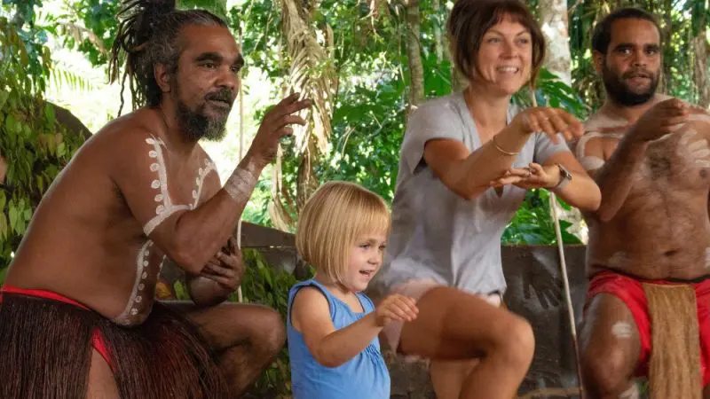 Four people, including a child, perform a vibrant traditional dance outdoors near the Express Kuranda Later Departure terminal.