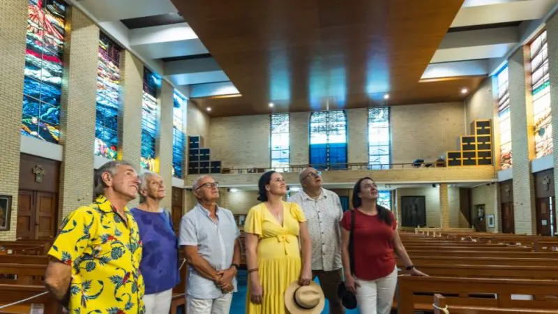 A group of six adults view stunning stained glass windows inside a historic church on the popular Cairns City Sights Green Island tour.