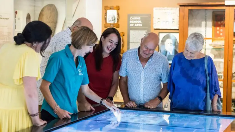 Six adults interact around a digital touchscreen exhibit at Cairns City Sights Green Island museum, exploring educational displays.