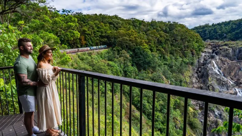 A couple shares a private moment on a balcony overlooking Kuranda’s lush gorge, cascading waterfall, and scenic railway views.