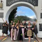 Eight performers in vibrant traditional Māori dress pose beneath a white archway after a Whakarewarewa Cultural Performance in New Zealand.