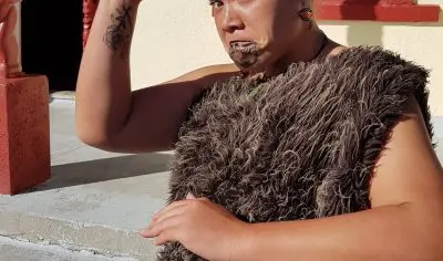 A Māori woman in authentic traditional attire welcomes visitors with a cultural gesture at Rotorua’s renowned Whakarewarewa performance.