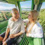 Happy couple riding a cable car over vibrant green hills on the 16-Day Best of East Coast Australia Tour from Sydney, scenic views.