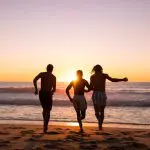 Three travellers run towards the sea at sunset during an epic 8 Day Sydney to Brisbane Fraser Island Comfort Tour adventure.