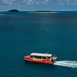 Vibrant red tour boat glides on clear blue ocean during 14 Day Sydney to Cairns Fraser Island Whitsundays Comfort Tour adventure.