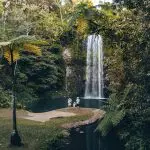 Three travellers at a scenic waterfall surrounded by lush rainforest, capturing highlights of a 14-day Sydney to Cairns tour.