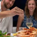 A traveller squeezes lemon over fresh prawns during a 14 Day Sydney to Cairns Tour with Fraser Island and Whitsundays highlights.