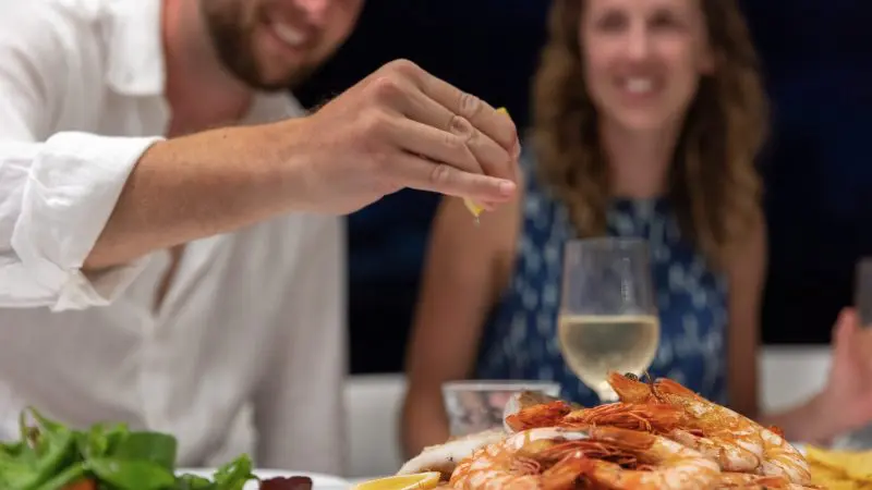 A traveller squeezes lemon over fresh prawns during a 14 Day Sydney to Cairns Tour with Fraser Island and Whitsundays highlights.