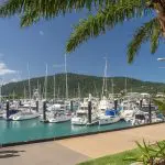 Travellers enjoy a scenic marina stroll past luxury yachts on the 14 Day Sydney to Cairns Tour, featuring Fraser Island and Whitsundays.