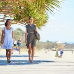 Two women walking barefoot on a sunlit boardwalk during a 14-day Sydney to Cairns with Fraser Island and Whitsundays Comfort Tour.