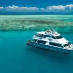 Luxurious white yacht anchored by a vibrant coral reef during the 14-Day Sydney to Cairns Fraser Island & Whitsundays Comfort Tour.