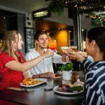 Four friends cheer with drinks at dinner, celebrating their 8-Day Sydney to Brisbane with Fraser Island Comfort Tour adventure.