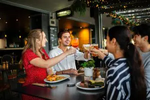 Four friends cheer with drinks at dinner, celebrating their 8-Day Sydney to Brisbane with Fraser Island Comfort Tour adventure.