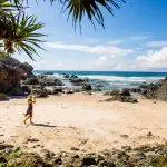 Traveller in a sunhat strolling along pristine sandy shores during the 16 Day Best of East Coast Australia Comfort Tour from Sydney.