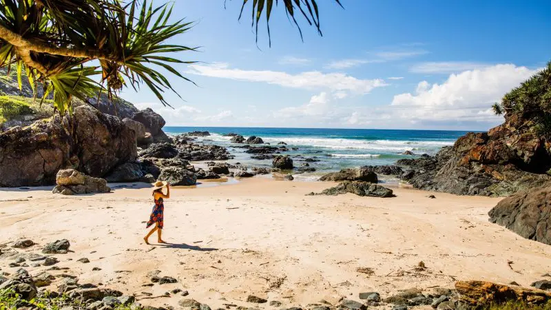 Traveller in a sunhat strolling along pristine sandy shores during the 16 Day Best of East Coast Australia Comfort Tour from Sydney.