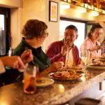 Four travellers relax at a stylish bar, sharing delicious food and lively stories from their 8 Day Sydney to Brisbane Fraser Island tour.