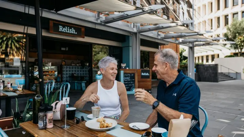 Smiling senior couple share coffee and pastries, happily recalling their 16 Day Best of East Coast Australia Comfort Tour experience.