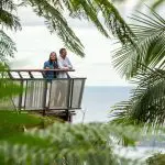 A couple stands on a balcony surrounded by lush plants, envisioning their dream 14 Day Sydney to Cairns Comfort Tour adventure.