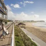 Surfers stroll along a scenic seafront promenade under clear skies during the 8 Day Sydney to Brisbane with Fraser Island Comfort Tour.