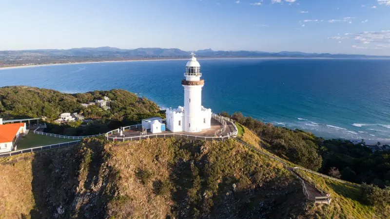 Iconic white lighthouse stands majestically atop lush grassy cliffs, a must-see attraction on the 8 Day Sydney to Brisbane tour.