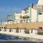 Crystal-clear outdoor swimming pool with marked lanes and a swimmer in a blue cap, ideal relaxation on East Coast Australia tours.