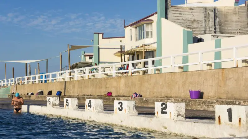 Crystal-clear outdoor swimming pool with marked lanes and a swimmer in a blue cap, ideal relaxation on East Coast Australia tours.