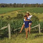 Happy couple enjoying a playful piggyback ride in a sunlit vineyard during their 8 Day Sydney to Brisbane Fraser Island Comfort Tour.