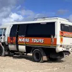 8 Day Sydney to Brisbane with Fraser Island Comfort Tour coach parked on pristine sandy beach by the sea, perfect coastal adventure.