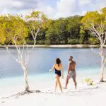 A man and woman walk along a scenic sandy lake beach, capturing the essence of a 14-Day Sydney to Cairns Comfort Tour adventure.