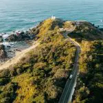 Scenic winding road curves towards a striking white lighthouse, evoking the 8 Day Sydney to Brisbane Fraser Island Comfort Tour experience.