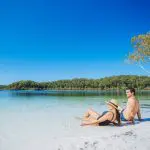 A couple enjoys a sunny sandy beach and crystal-clear blue water on the 8 Day Sydney to Brisbane with Fraser Island Comfort Tour.