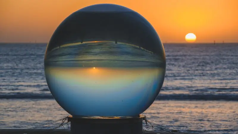 Crystal clear glass sphere on sandy Ningaloo Reef beach mirrors a vivid, upside-down sunset, showcasing unique coastal beauty.