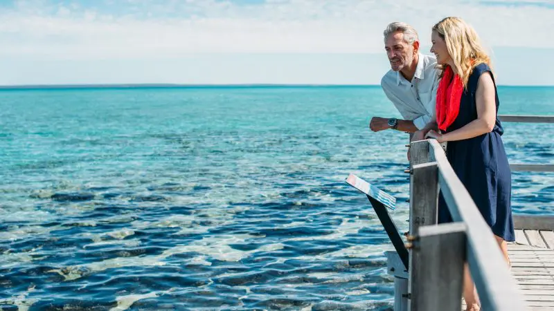 A happy couple stands on a scenic wooden pier, envisioning the 8 Day Perth to Exmouth Comfort Tour and Ningaloo Reef experiences.