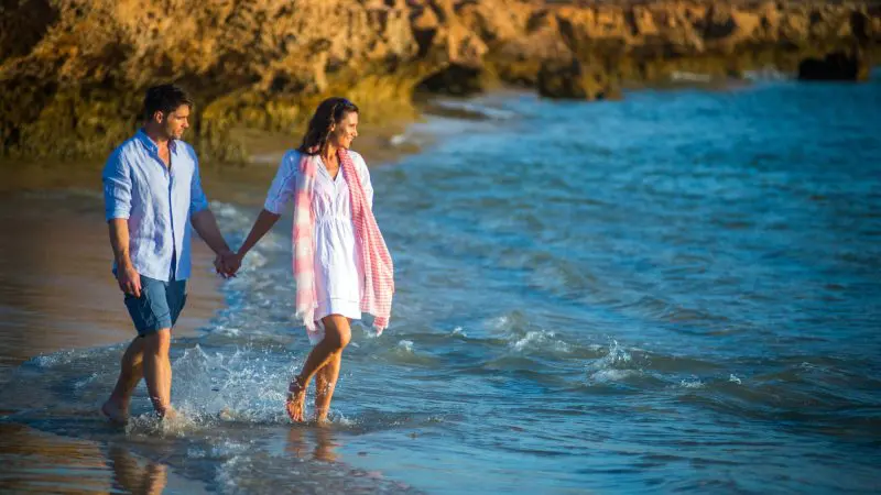 A joyful couple walks hand in hand along the pristine Perth to Exmouth coast, enjoying scenic views on their 8 Day Comfort Tour.