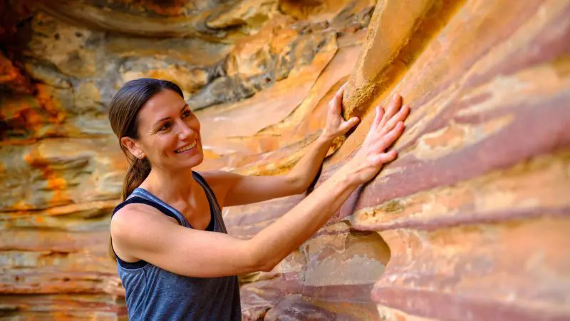 Smiling woman in a vest explores vibrant, multicoloured rock formations on the 8 Day Perth to Exmouth Comfort Tour adventure.