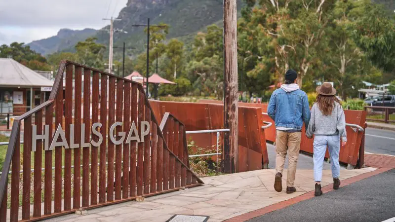 Couple walk hand in hand by the Halls Gap sign, enjoying stunning views on a 1 Day Grampians Eco Wilderness Escape tour.