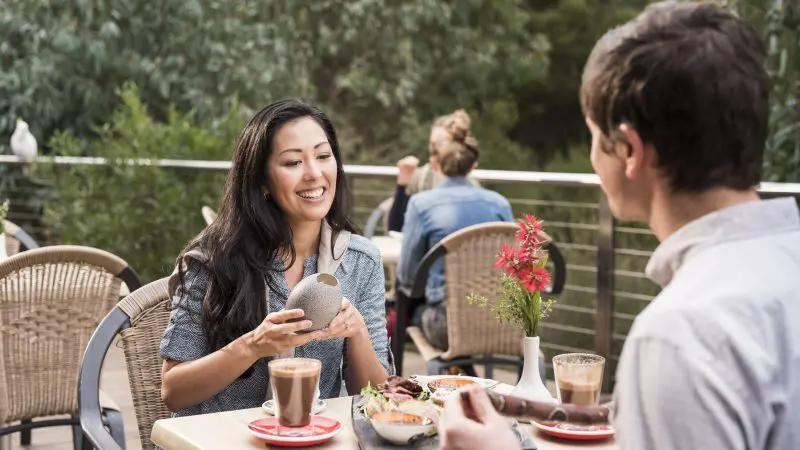 A man and woman savour gourmet meals and drinks at a scenic outdoor café, reliving their 1 Day Grampians Eco Wilderness Escape tour.