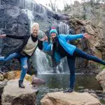 Two women enjoying a playful moment on rocks by a stunning Grampians waterfall during their 1 Day Eco Wilderness Escape adventure.