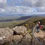 A woman wearing a stylish hat enjoys breathtaking panoramic views from a scenic lookout on a Grampians Eco Wilderness Escape tour.