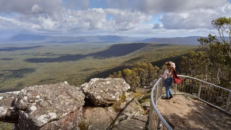 A woman wearing a stylish hat enjoys breathtaking panoramic views from a scenic lookout on a Grampians Eco Wilderness Escape tour.